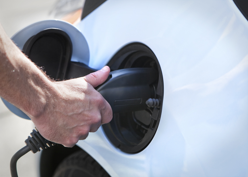 A hand plugging in an electric car charger.